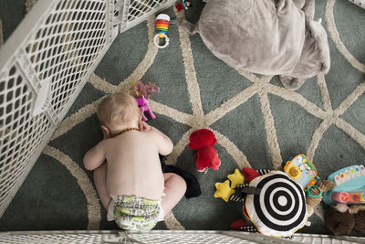 High angle view of shirtless baby boy playing with toys while bending on carpet at home