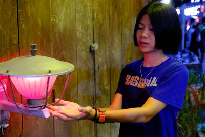 Young woman standing by lighting equipment on wooden wall