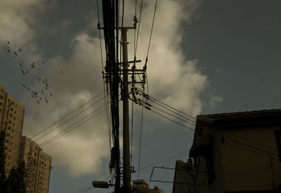 Low angle view of electricity pylon against cloudy sky