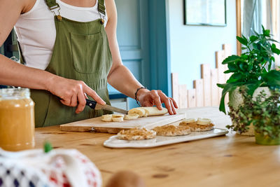 Woman making healthy breakfast or brunch, cutting banana for sandwich with spread peanut butter. 