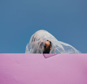 Low angle portrait of man relaxing on snow against blue sky