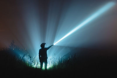 Man with illuminated flash light standing on field against sky at night