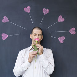 Man smelling flower against blackboard