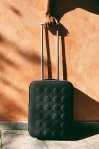 Cropped image of hand pulling luggage against wall