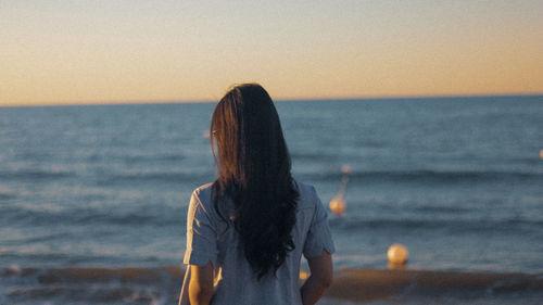 Woman looking at sea against sky during sunset