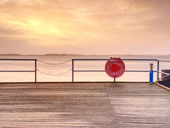 Red pier over sea against sky during sunset