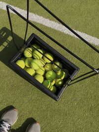 Low section of man standing by tennis balls in container at court during sunny day