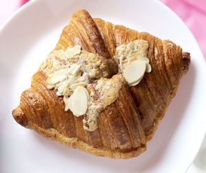Almond croissant for breakfast on white plate with yellow green background, flat lay, top view.