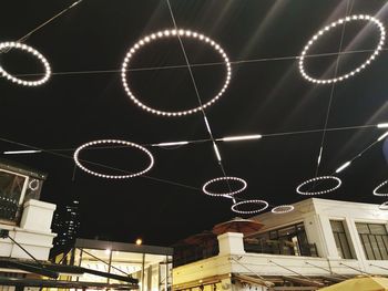 Low angle view of illuminated lighting equipment on building at night