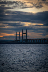 Silhouette bridge over sea against sky during sunset