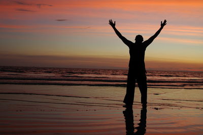 Silhouette man standing on beach against sky during sunset