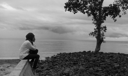 Woman sitting on beach against sky