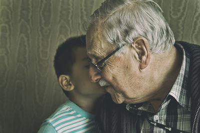 Close-up of grandfather and grandson against wall at home