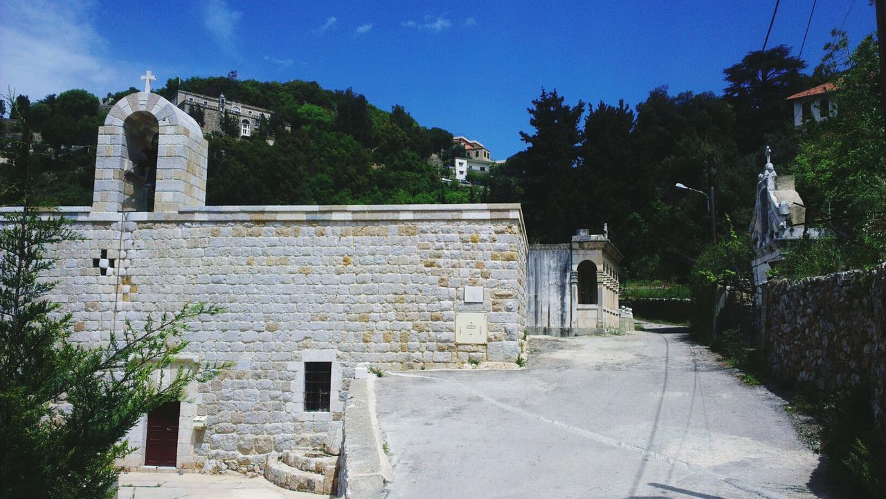 architecture, built structure, building exterior, tree, history, old, sky, stone wall, sunlight, the past, old ruin, day, arch, the way forward, stone material, house, no people, outdoors, blue, wall - building feature