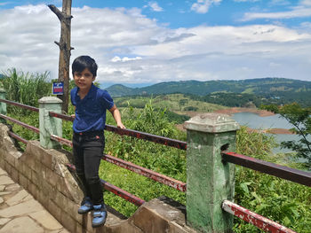 Portrait of boy standing on railing against mountain