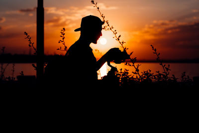 Silhouette man standing by lake against sky during sunset