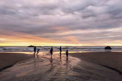 Silhouette people standing on beach against sky during sunset