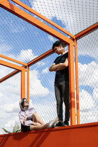 Teenage couple looking at each standing and sitting on fenced bridge
