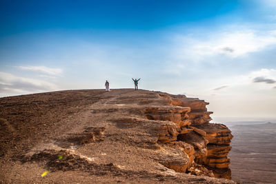 Two people standing on mountain against sky during sunny day