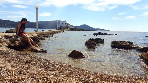 Woman standing on rock by sea against sky