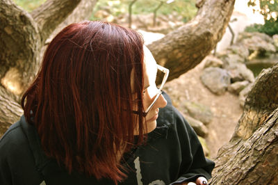 Close-up of young woman looking away by tree trunk