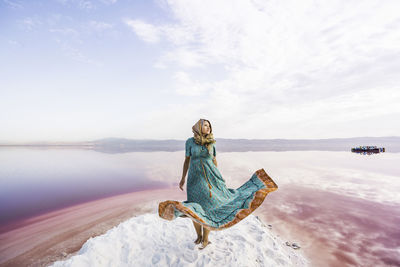 Woman with umbrella at sea shore against sky