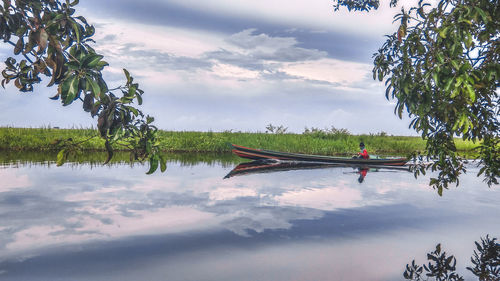 Mature man in boat on river against cloudy sky