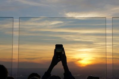Low angle view of hand holding camera against sky during sunset