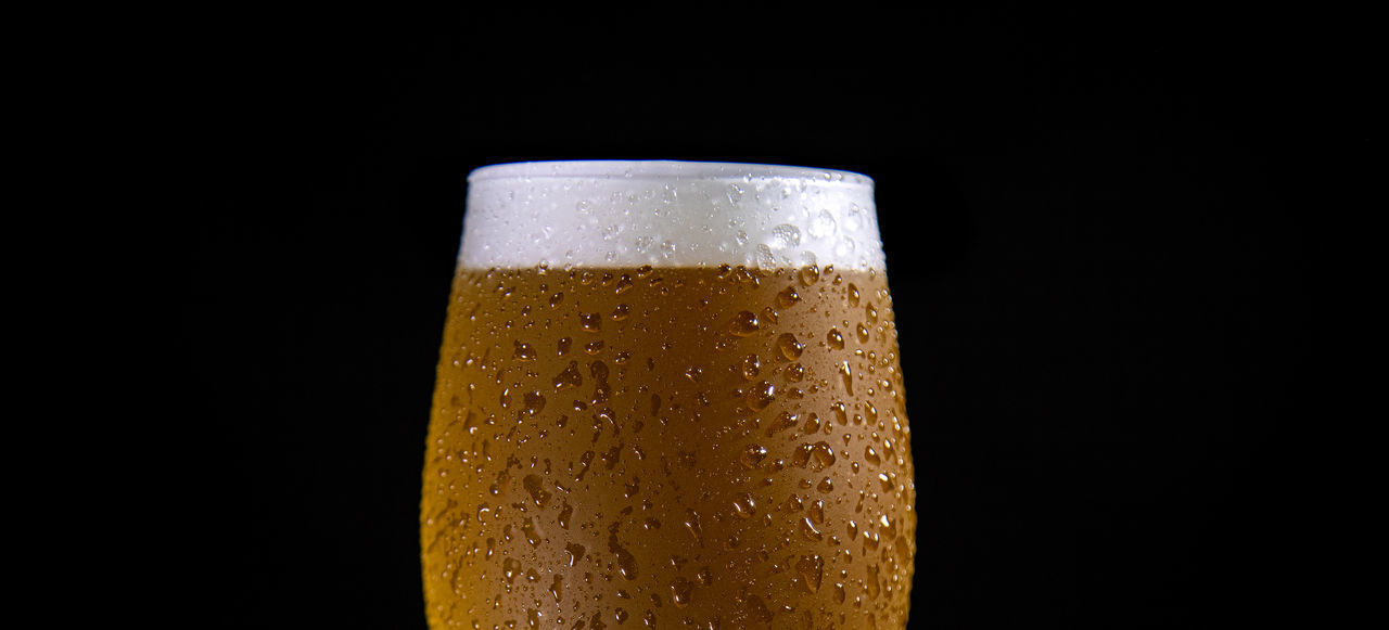 CLOSE-UP OF GLASS OF BEER OVER BLACK BACKGROUND