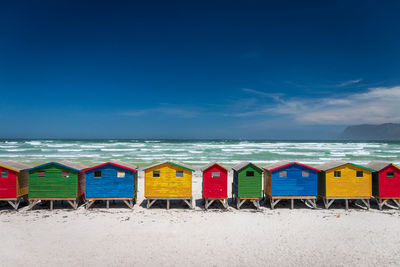 Multi colored beach huts on shore against blue sky