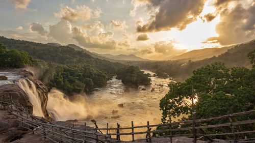 Scenic view of waterfall by river against sky during sunset