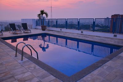 Chairs and table by swimming pool against sky during sunset