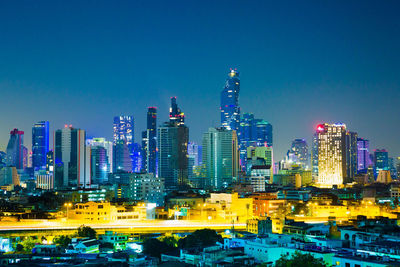 Illuminated buildings in city against blue sky