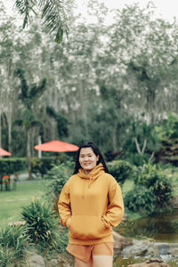 Portrait of young woman standing against trees