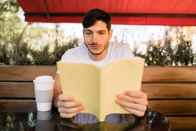 Young man reading book sitting at cafe