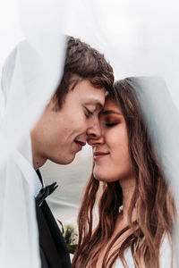 Close-up of newlywed couple with eyes closed romancing under veil