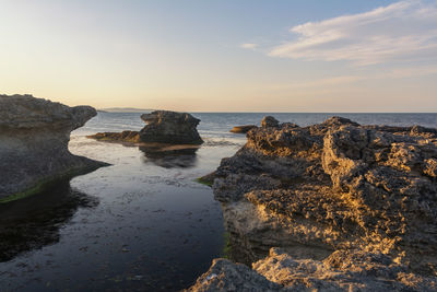 Rocks on beach against sky during sunset