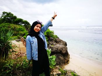 Portrait of young woman gesturing peace sign while standing at beach