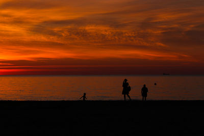 Silhouette people on beach against sky during sunset