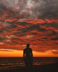 Silhouette man looking at sea against orange sky