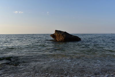 Rock formation in sea against sky during sunset