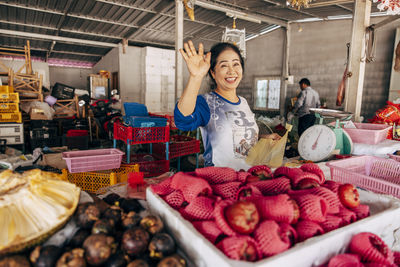 Portrait of smiling female vendor waving at stall