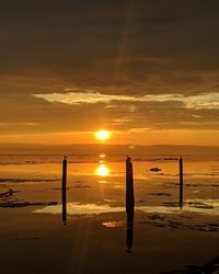 Silhouette wooden post on beach against sky during sunset