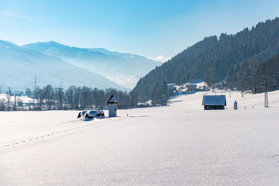 Winter landscape a snow-covered field, mountains in background. blue sky and road leading to chapel