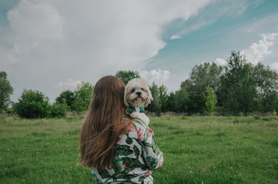 Girl standing by tree on field against sky