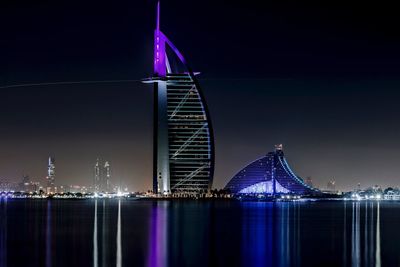 Illuminated burj al arab hotel by sea against sky in city at night