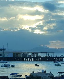 Boats moored at harbor against cloudy sky