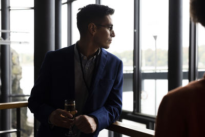 Businessman having wine while looking through window at convention center