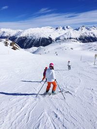 Rear view of people skiing on snowcapped mountain against sky