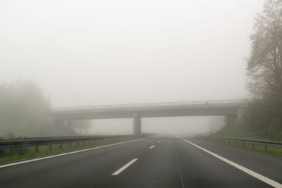 Road by trees against sky during foggy weather